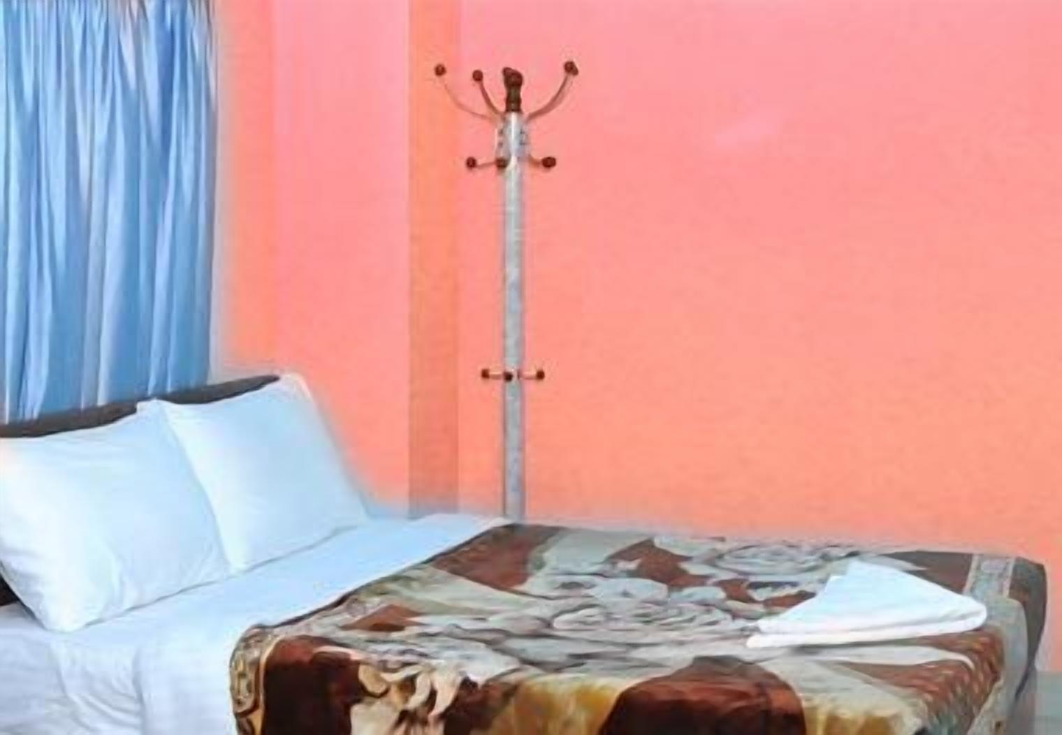 A bed with white linens, a floral-patterned bedspread, and a coat rack against a pink wall.