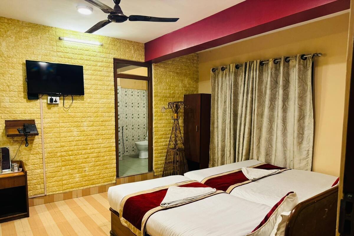 A hotel room with a large bed, a TV mounted on the wall, a telephone, and a mirror.