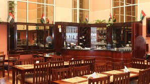 A restaurant with wooden tables and chairs, a bar area with shelves of glassware, and flags on the walls. - Mount Royal Hotel (Dubai)