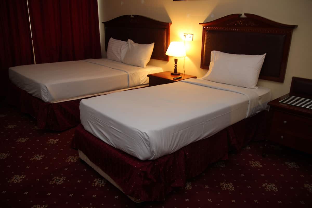 A hotel room with two single beds, a nightstand with a lamp, and a red carpeted floor.