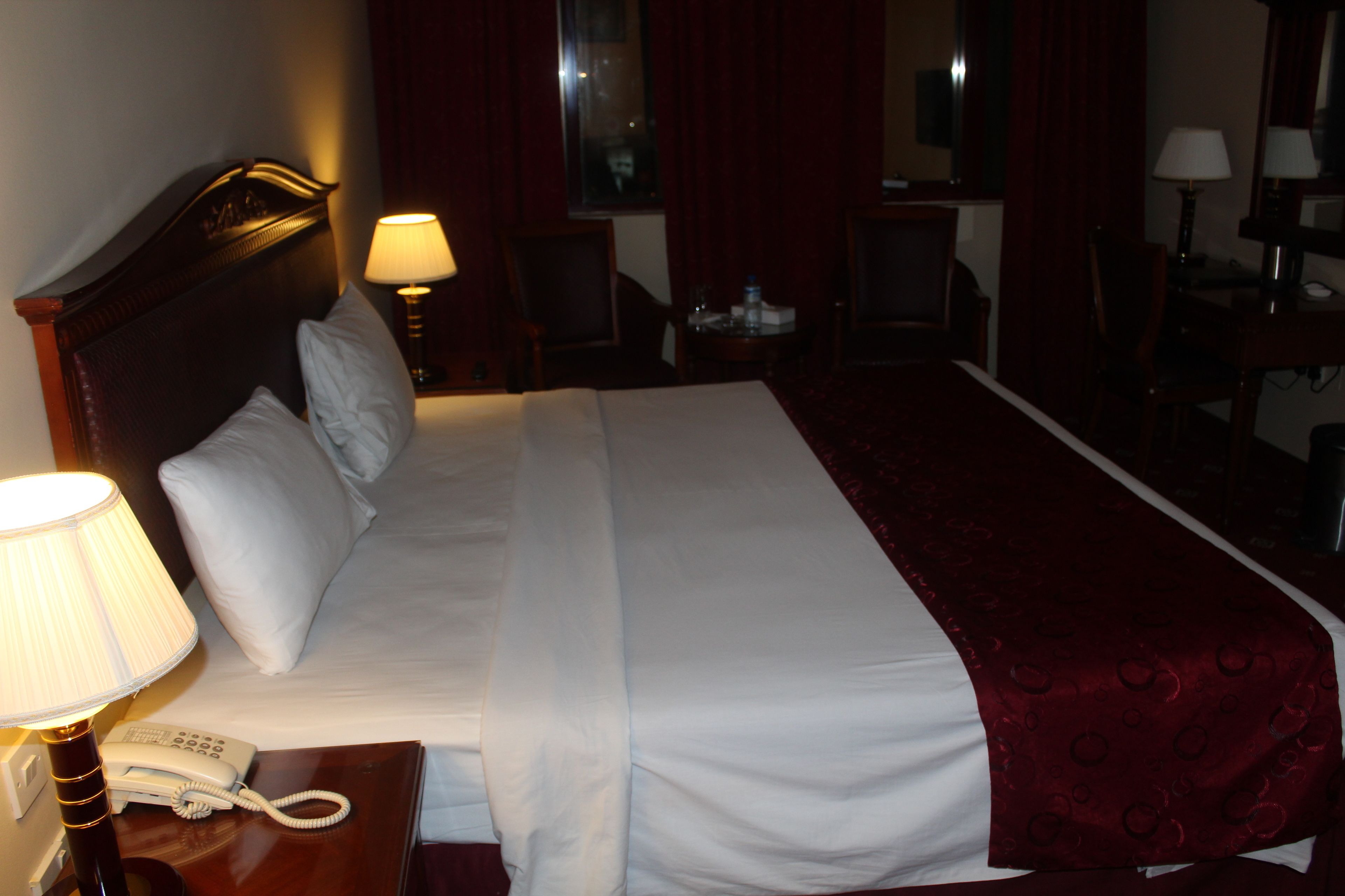 Una habitación de hotel con una cama grande, un teléfono en la mesita de noche, una lámpara y un escritorio con una silla.