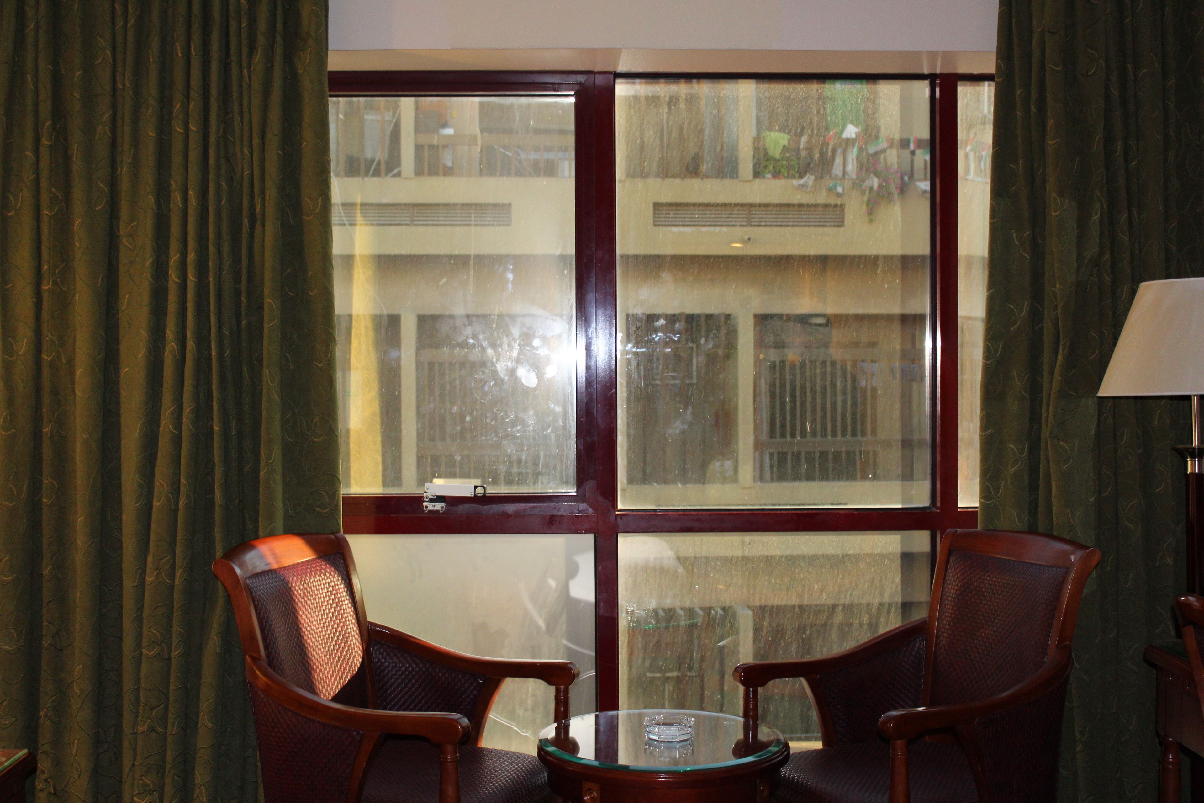 A room with two wooden chairs, a glass table, and a large window with curtains.