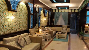 A hotel lobby with a sofa, armchairs, a coffee table, and a small table with a lamp.