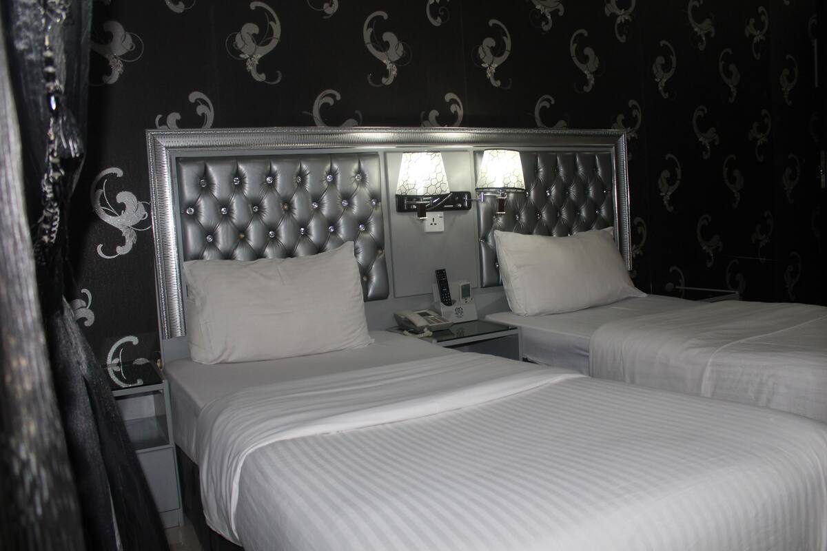A hotel room with two beds, a large tufted headboard, bedside lamps, and a telephone.