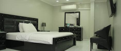 A modern bedroom with a large bed, a dresser, a chair, and a TV.