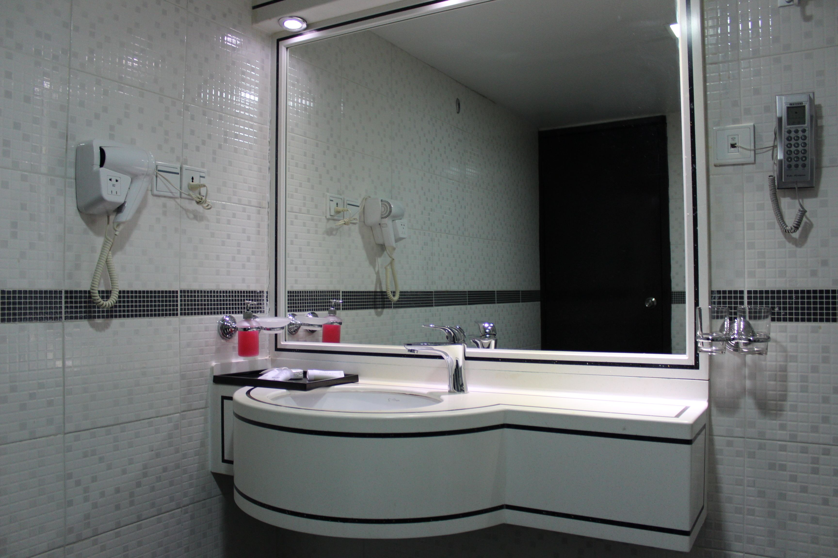 A bathroom with a white sink, a mirror, and a hairdryer mounted on the wall.
