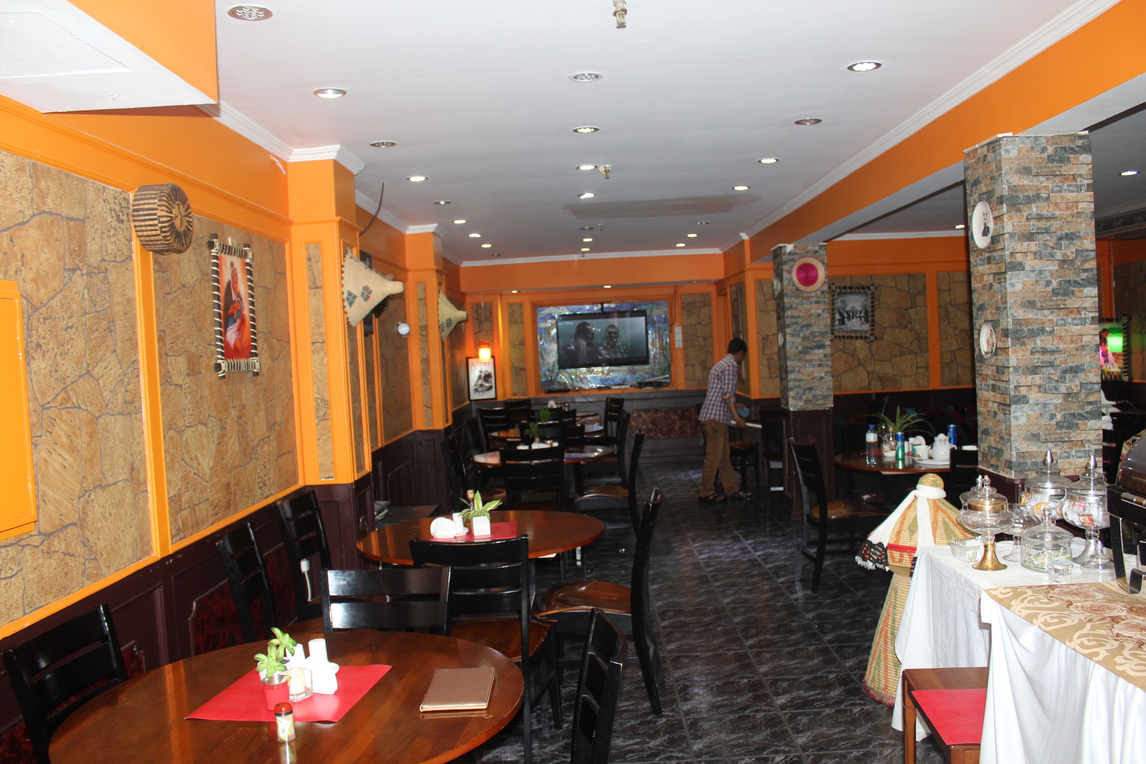 A restaurant with multiple tables and chairs, a television screen, and decorative elements on the walls.