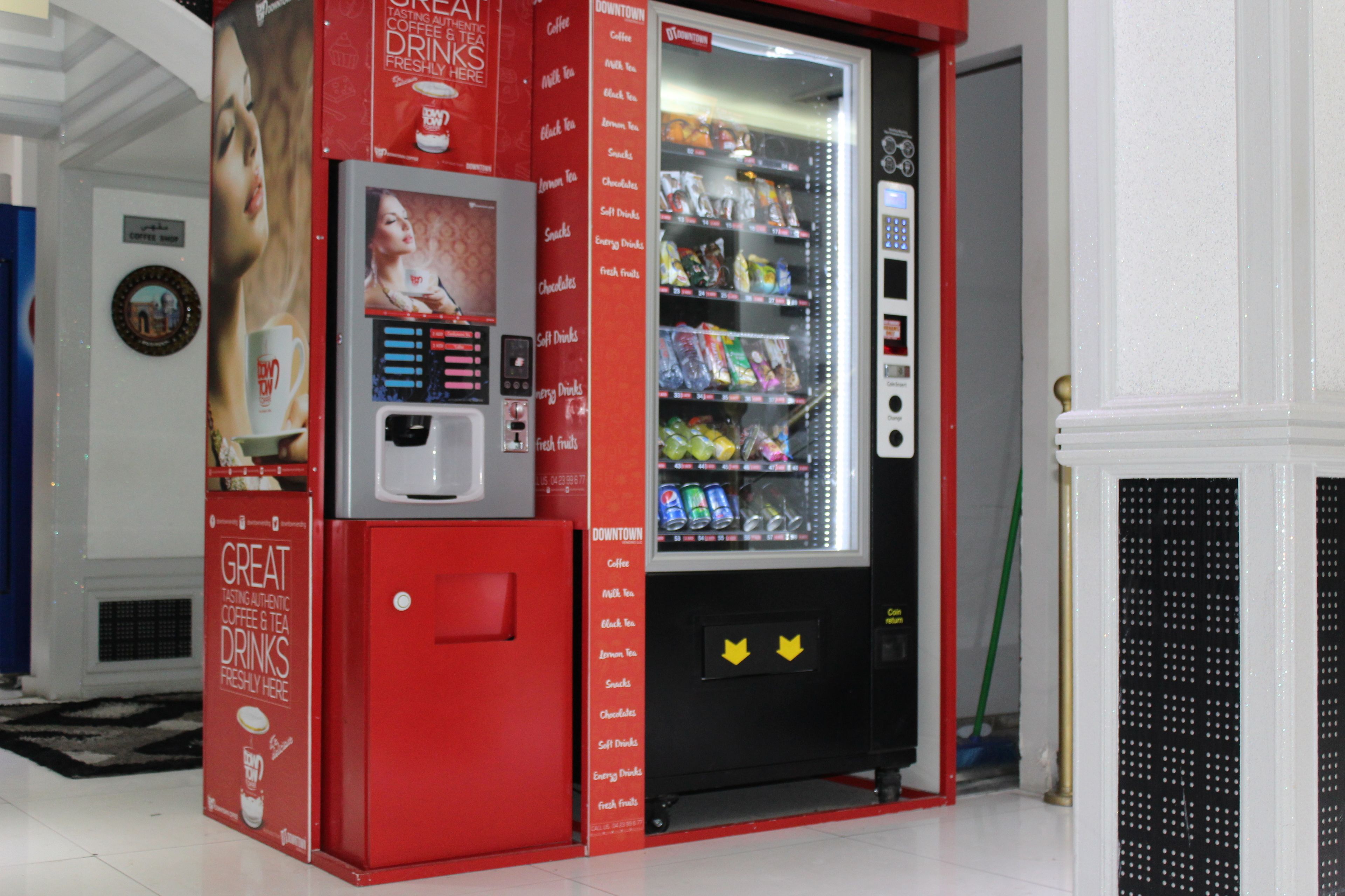 Una màquina expenedora vermella amb dosificador de cafè i te, panell de selecció de begudes i secció refrigerada amb aperitius i refrescos.