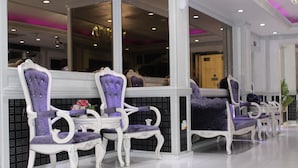 A reception area with white and purple upholstered chairs, a white reception desk, and a large mirror reflecting the interior. - White Fort Hotel (Dubai)