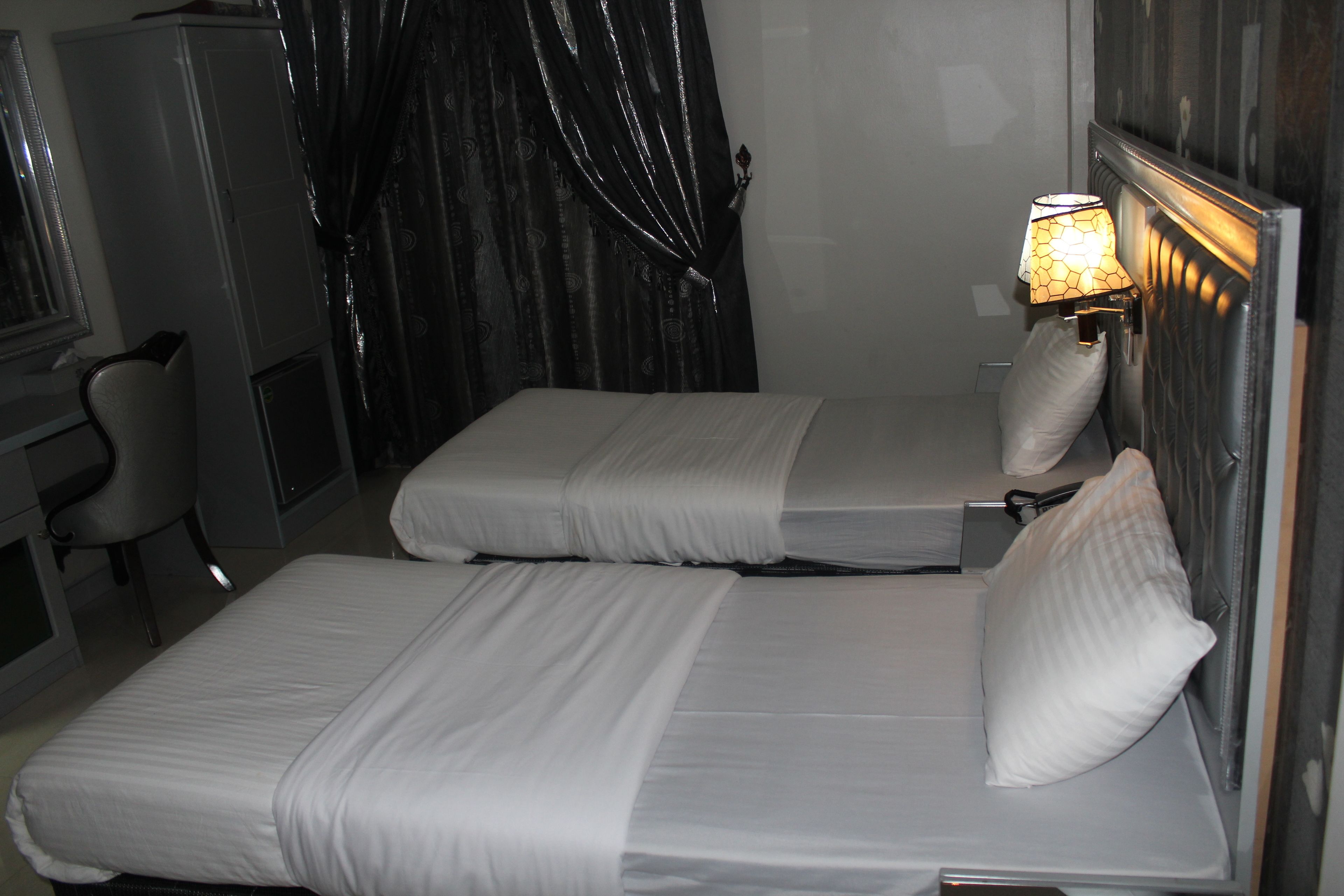 A hotel room with two single beds, a desk, a chair, and a lamp.