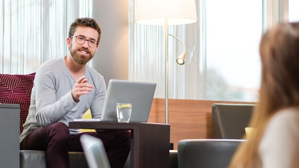 A man sitting on a couch with a laptop, a woman sitting on the floor, and a lamp in the background. - MASEVEN Stuttgart SI-Centrum (ehem. SI-SUITES) (Stuttgart)