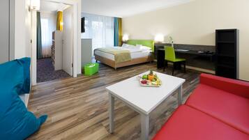 A hotel room with a bed, a desk, a chair, a table with fruit, and a red couch.