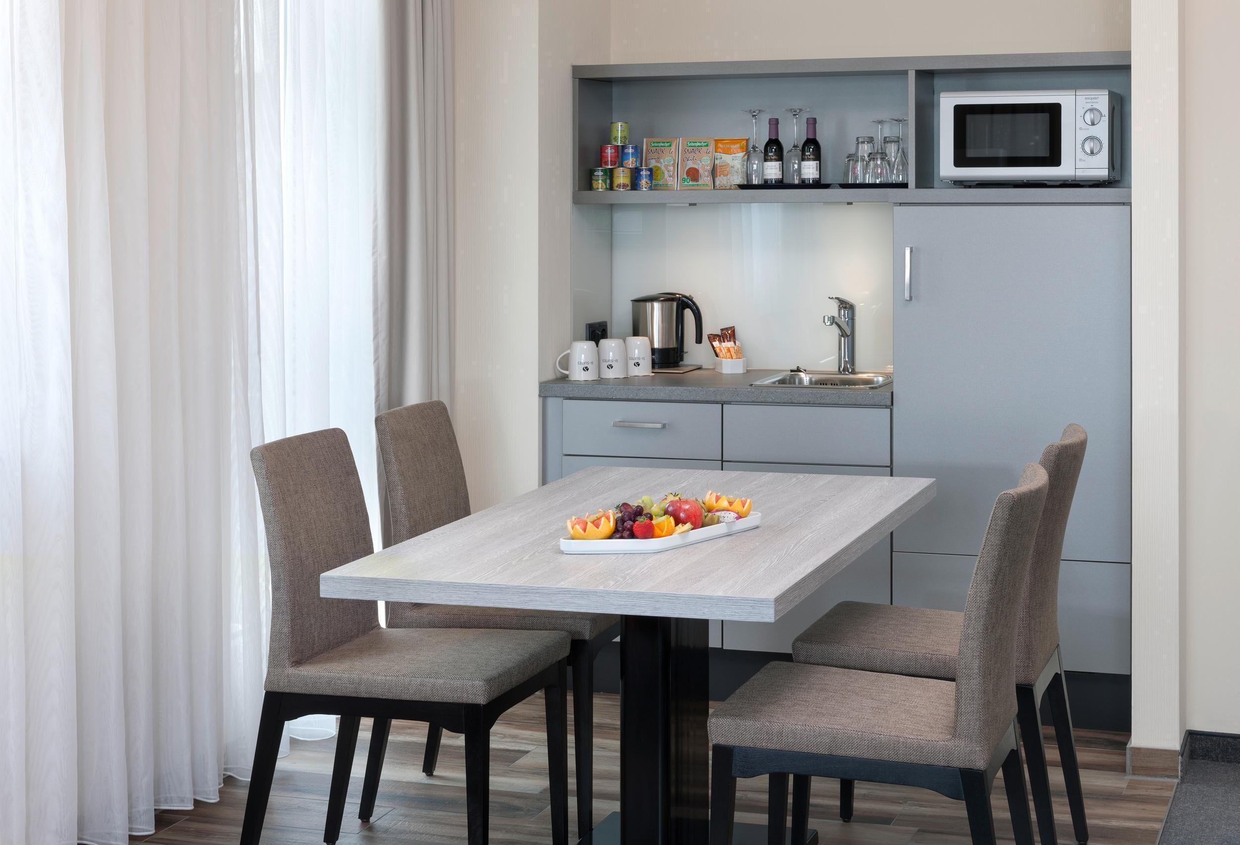A modern kitchen with a dining table, chairs, and a microwave above the counter.