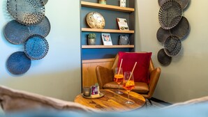 Un coin salon accueillant avec un fauteuil en cuir, une petite table en bois sur laquelle sont posées des boissons, et des assiettes décoratives accrochées aux murs.