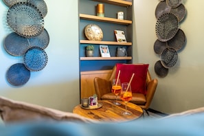 Een gezellige zithoek met een lederen fauteuil, een klein houten tafeltje met drankjes en decoratieve borden aan de muur.