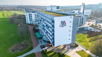 A modern building with a rooftop garden, a large sign for 'MASEVEN', and a parking area.