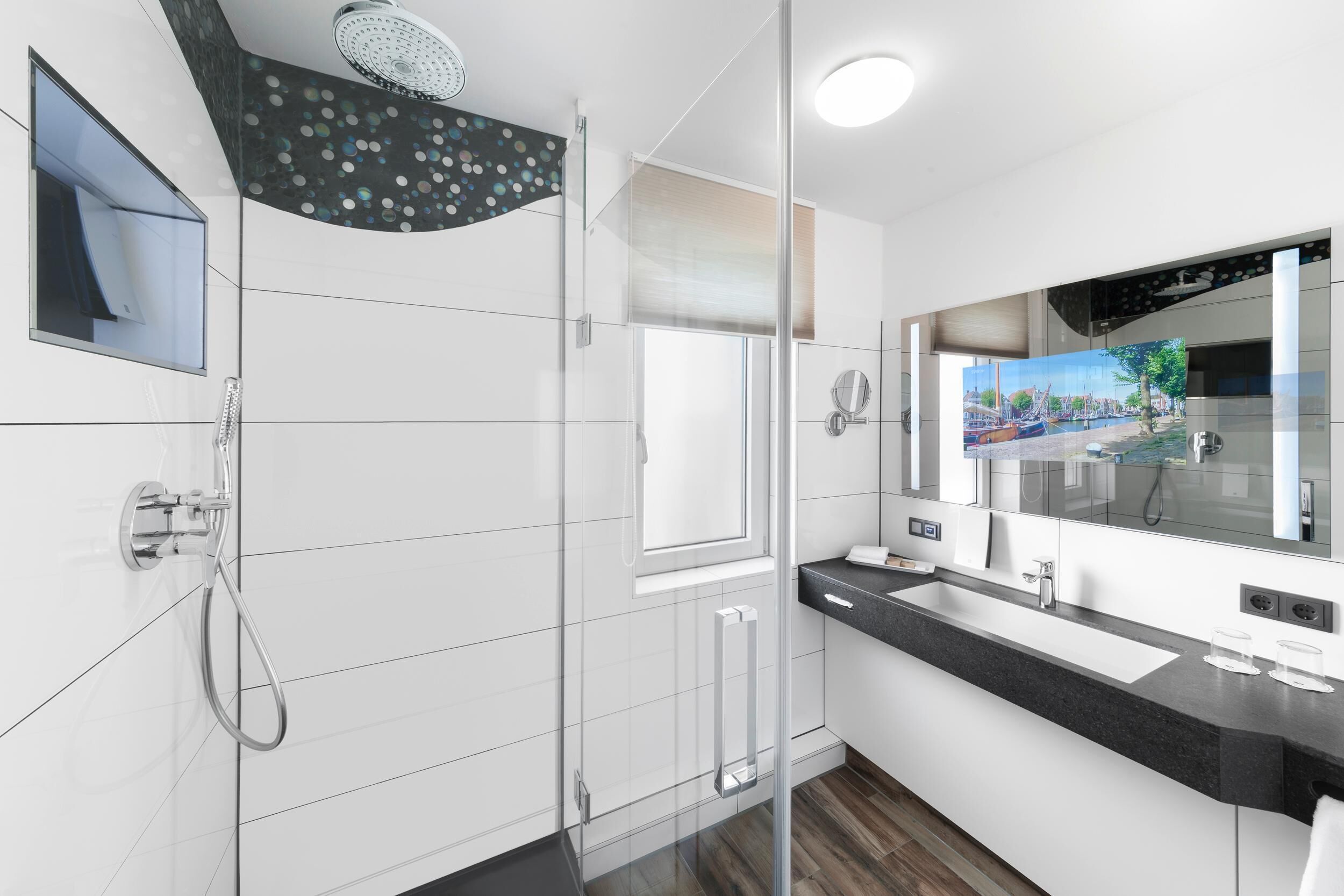 Un baño moderno con cabina de ducha de vidrio, un espejo grande y vistas a un canal por la ventana.