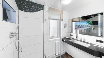 Un baño moderno con cabina de ducha de vidrio, un espejo grande y vistas a un canal por la ventana.
