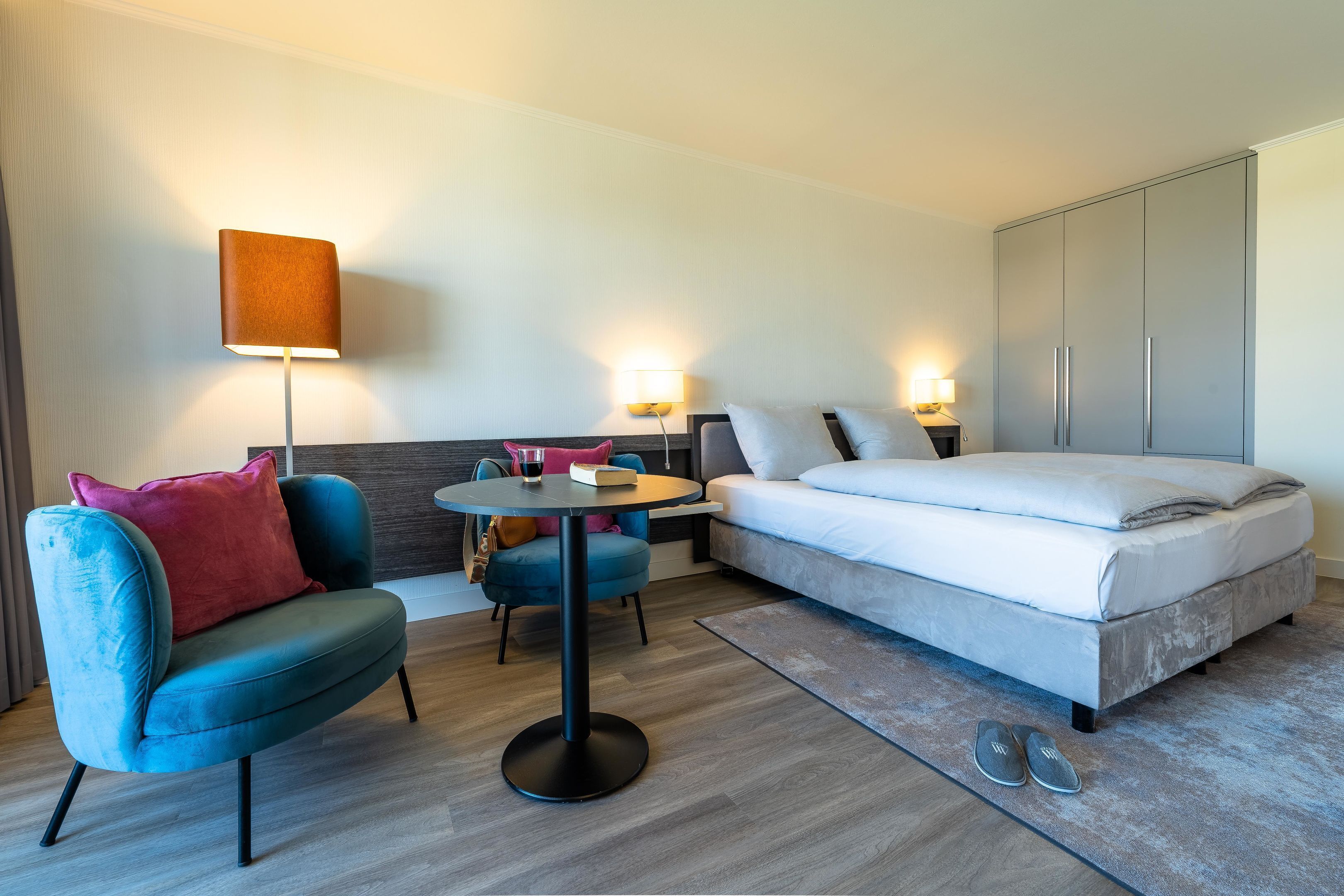 Una habitación de hotel con cama, sofá, una mesita, lámpara y armario.