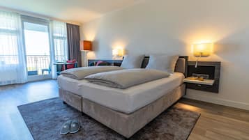 A modern hotel room with a large bed, a small table, two bedside lamps, and a balcony with a view.