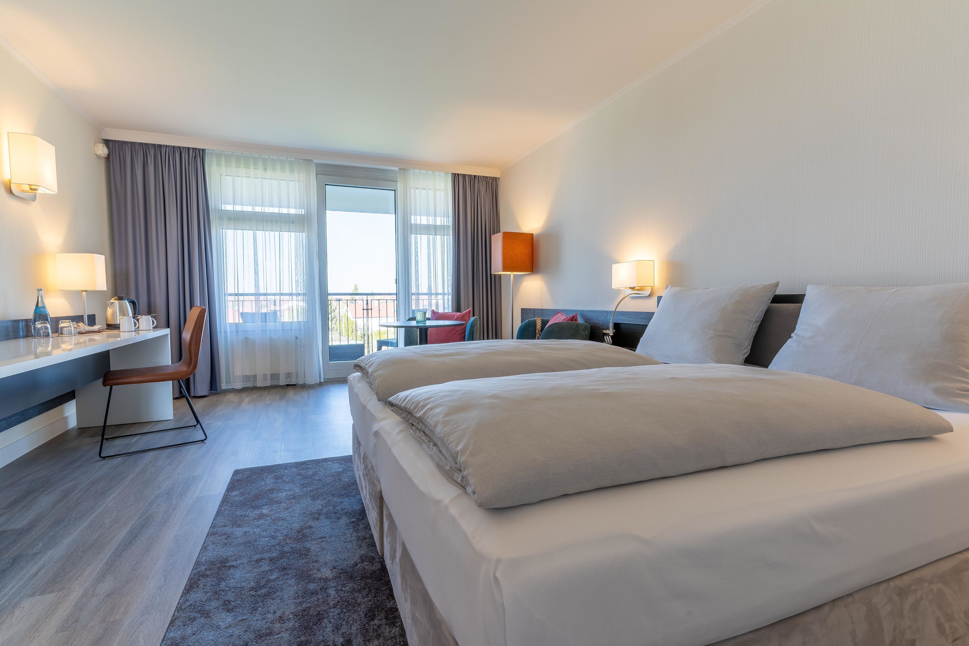 A hotel room with a large bed, a desk, a chair, and a balcony with a view.