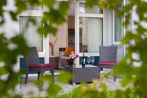 A modern living room with wicker furniture, a glass coffee table, and a vase of flowers. - MASEVEN Stuttgart SI-Centrum (ehem. SI-SUITES) (Stuttgart)