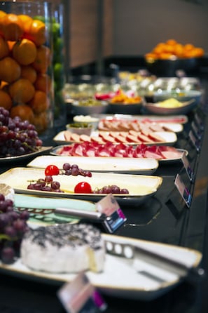 Una mesa de buffet con diferentes alimentos, incluyendo frutas, quesos y embutidos.