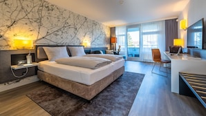 A modern hotel room with a large bed, bedside tables, a desk, and a view of the outdoors.
