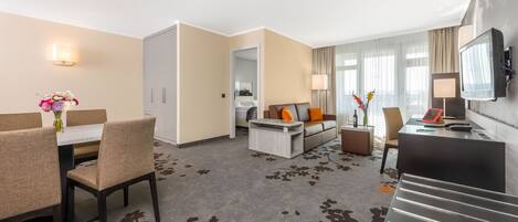 Una habitación de hotel con comedor, sofá, televisor y escalera.