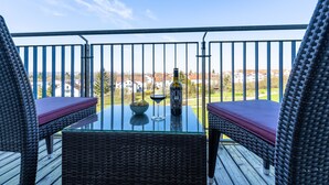 A balcony with wicker furniture, a glass table, and a bottle of wine.