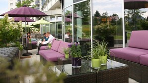 A modern outdoor seating area with purple sofas and green planters, overlooking a residential area. - MASEVEN Stuttgart SI-Centrum (ehem. SI-SUITES) (Stuttgart)