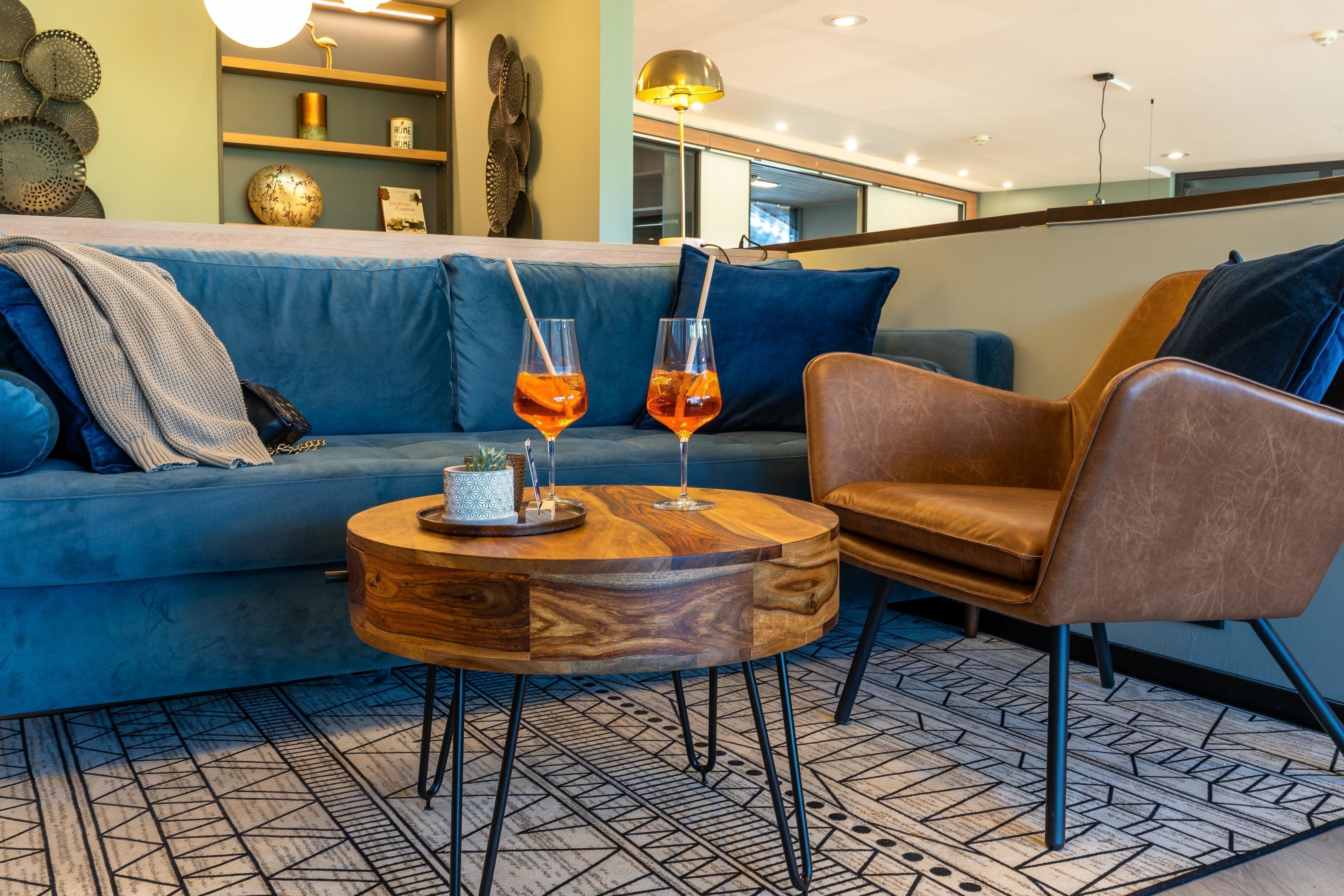 Ein modernes Wohnzimmer mit einem blauen Sofa, einem Holztisch und einem braunen Ledersessel. Auf dem Tisch stehen zwei Gläser Orangensaft.