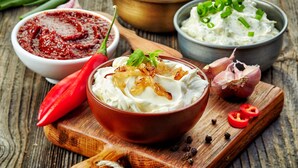 A bowl of creamy dip garnished with onions and herbs, accompanied by a red chili pepper, garlic, and sliced tomatoes on a wooden board. - MASEVEN Stuttgart SI-Centrum (ehem. SI-SUITES) (Stuttgart)
