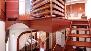A multi-level wooden staircase with a curved design, connecting different floors of a room with a bed and a small table. - Dar Loulema (Essaouira)