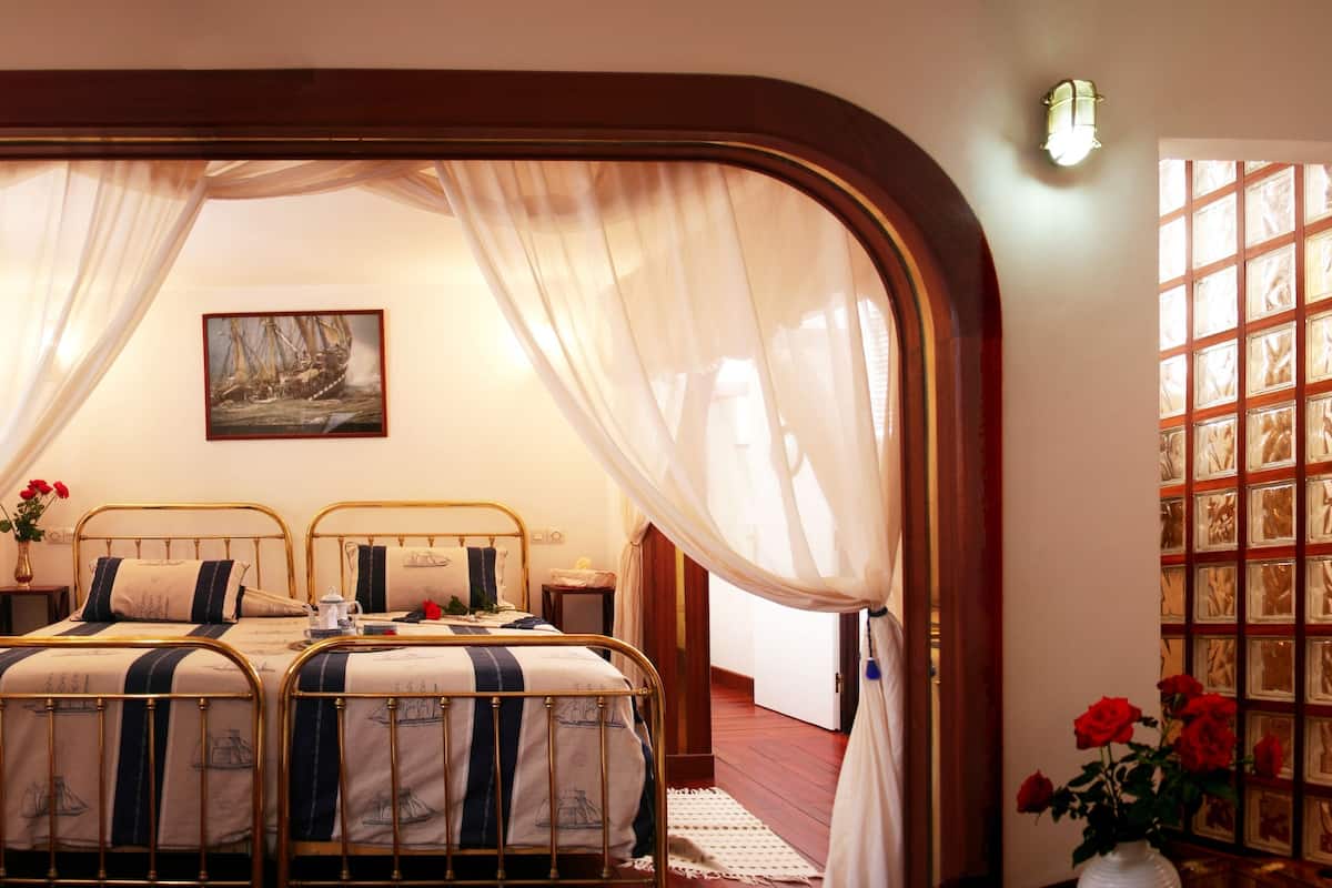 A bedroom with two beds, a painting on the wall, and a window with curtains.