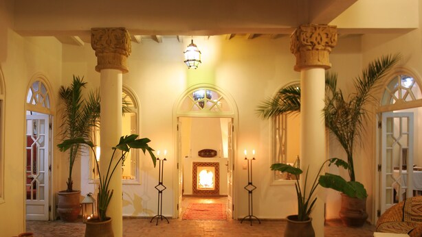 A hallway with a fountain, potted plants, and candle stands. - Dar Loulema (Essaouira)