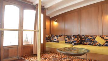 A room with a wooden door, a patterned rug, a sofa with colorful cushions, and a glass coffee table.