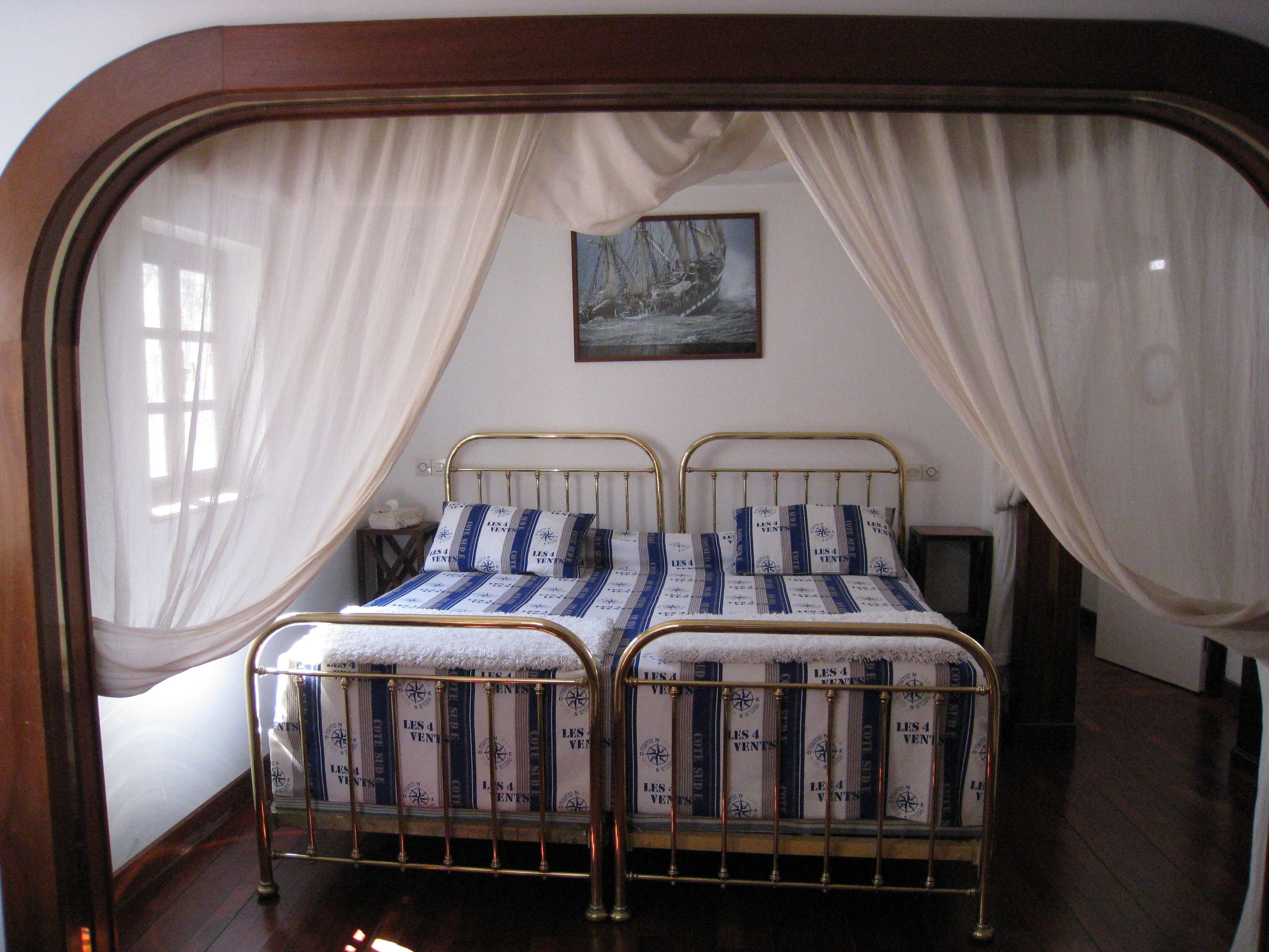 A double bed with a metal frame and a canopy, a small bedside table, and a painting on the wall.