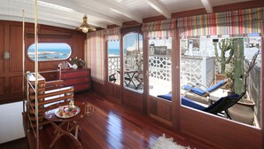 A wooden interior with a dining area, a view of the sea through a window, and a balcony with a cactus. - Dar Loulema (Essaouira)