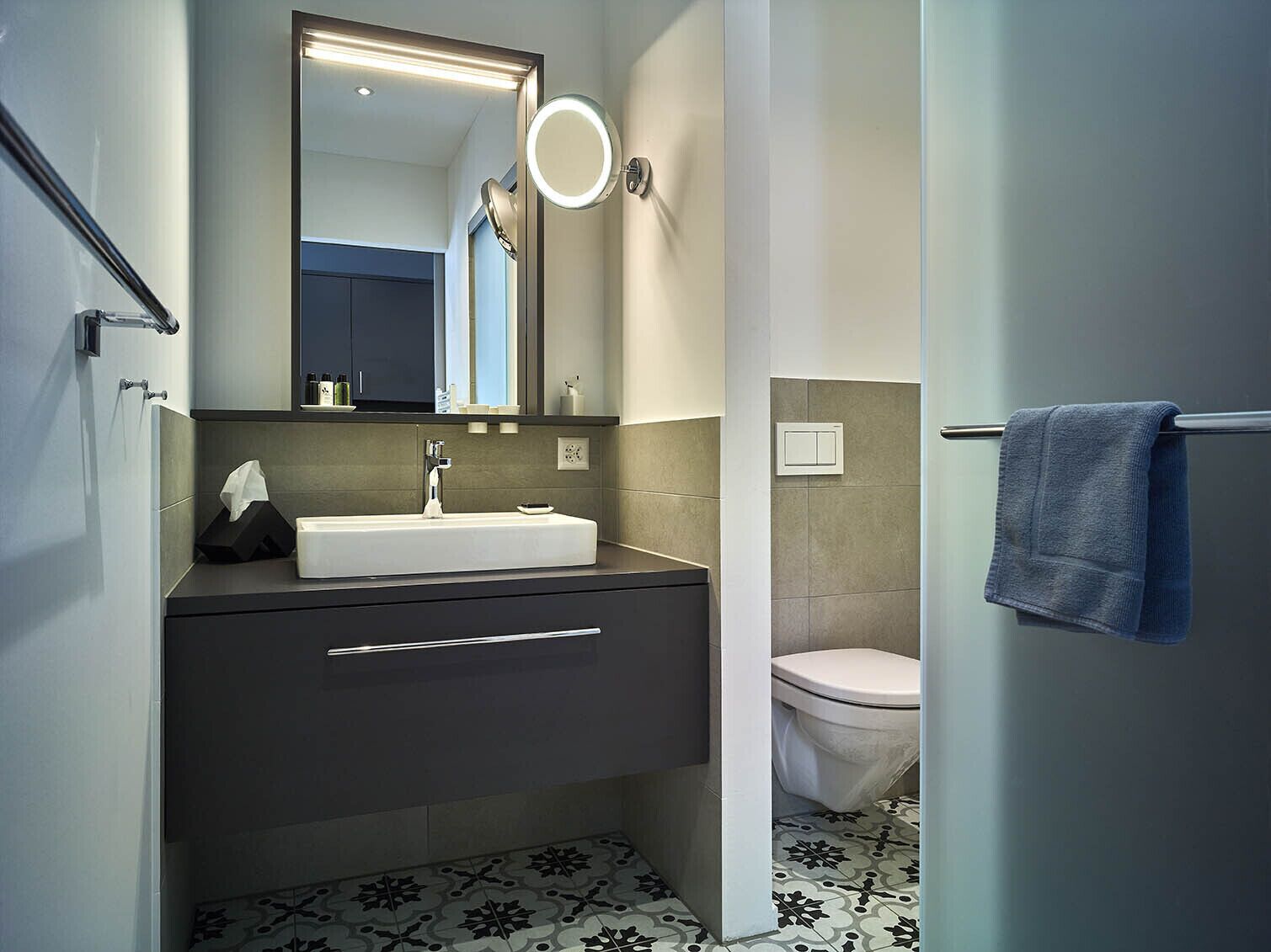 Ein modernes Badezimmer mit einem weißen Waschbecken, einer dunklen Kommode und einer Toilette.