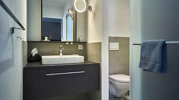 Ein modernes Badezimmer mit einem weißen Waschbecken, einer dunklen Kommode und einer Toilette.