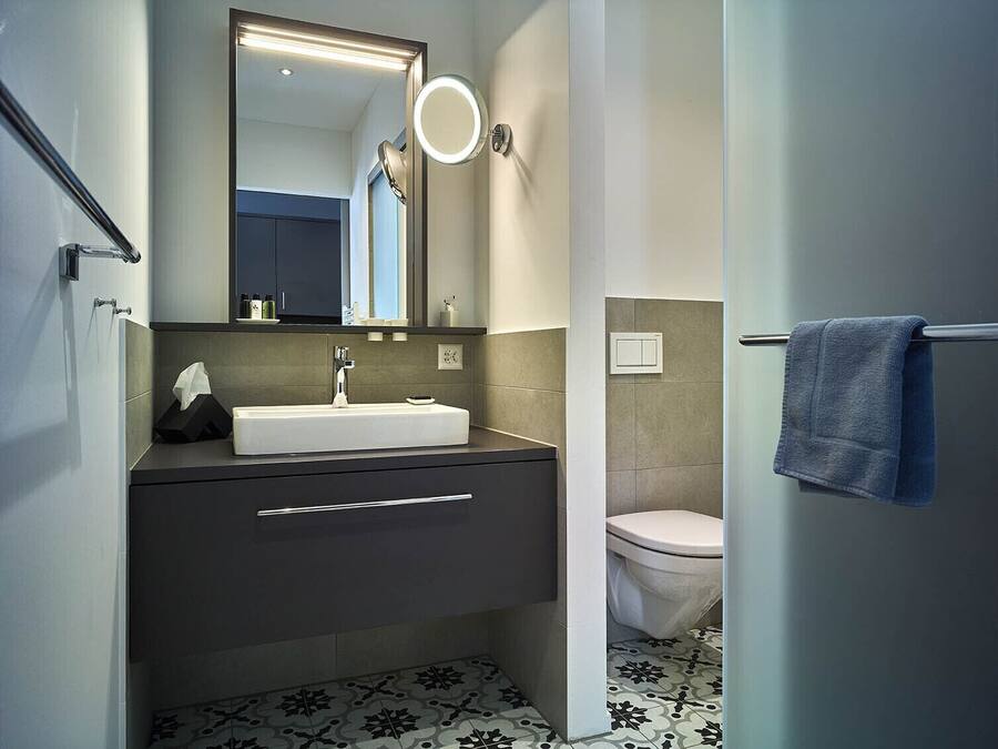 Un baño moderno con un lavabo blanco, tocador oscuro y un inodoro.