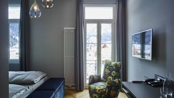 Un dormitorio moderno con cama, una silla, un radiador, un televisor y vistas a montañas nevadas.