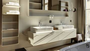 A modern bathroom with two sinks, a large mirror, and a built-in shelf with towels.