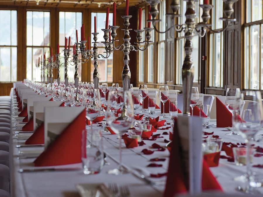 Une longue table à manger, dressée avec de nombreux couverts, comprenant des verres à vin et des serviettes rouges.