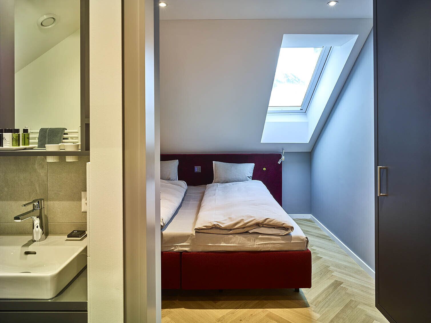 Un dormitorio moderno con tragaluz, cabecera roja y suelo de madera.