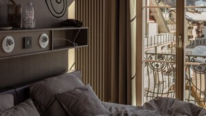 A bedroom with a bed, a shelf with items, a radiator, and a window with a view of buildings. - Bellevue-Terminus - Urban Lifestyle Hotel (Engelberg)