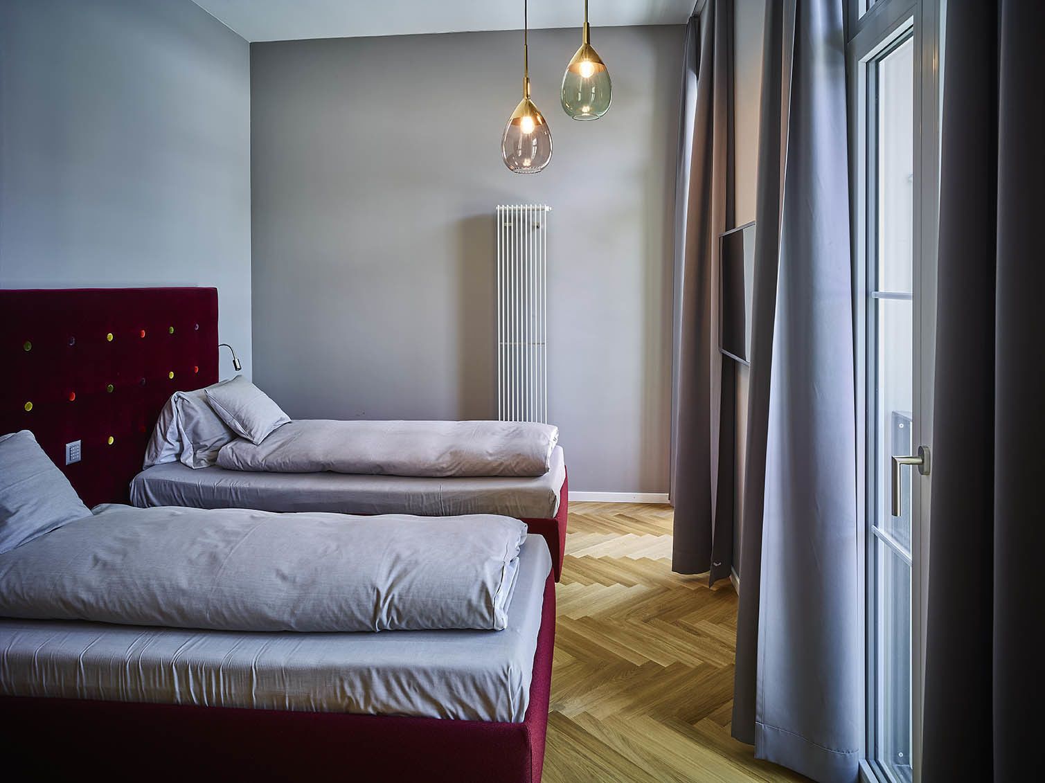 A modern bedroom with two beds, a radiator, and a window with curtains.