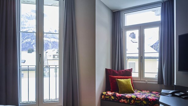 Un dormitorio con cama, escritorio con teléfono y ventanas grandes con cortinas.