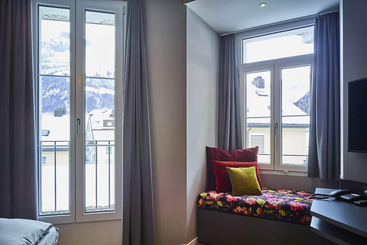 Un dormitorio con cama, escritorio con teléfono y ventanas grandes con cortinas.